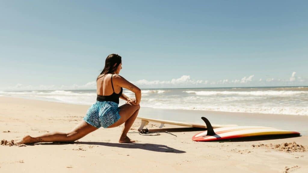 An image of a surfer on a beach stretching before going out to surf to prevent injury