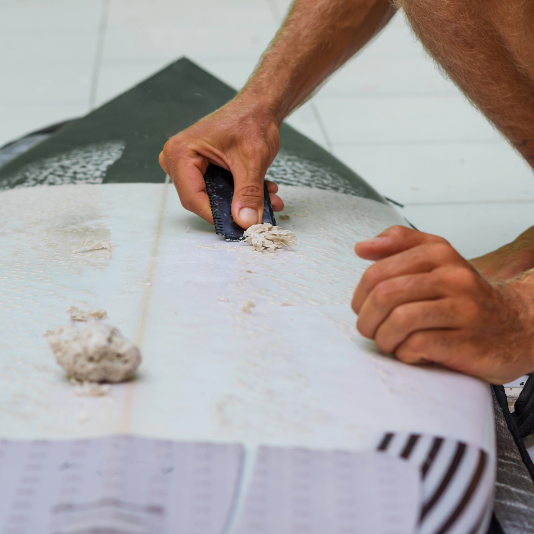 A man scrapes wax off of his surfboard