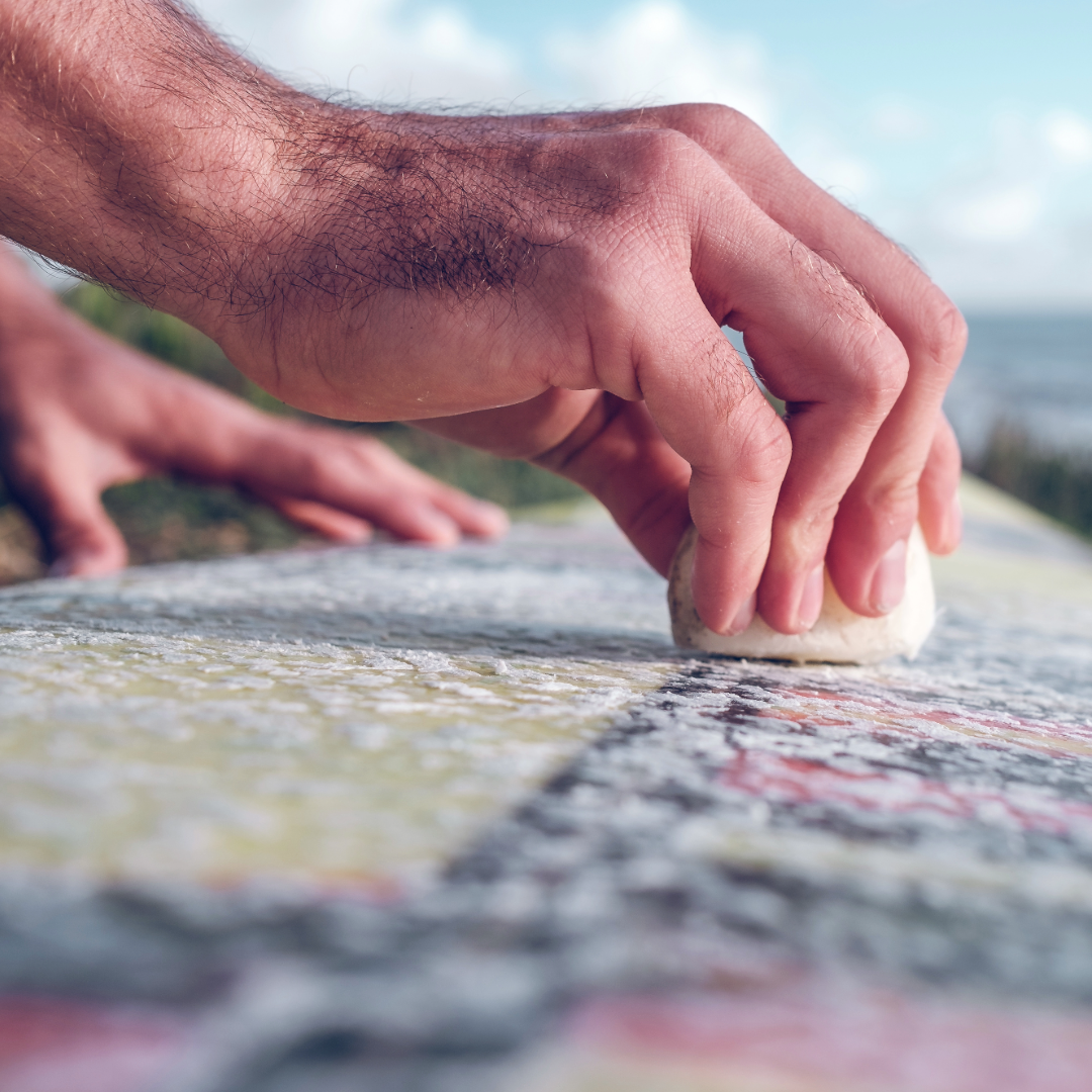 A man displays how to wax a surfboard