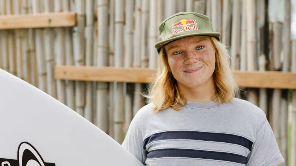 An image of caitlin simmers holding a surfboard wearing a red bull hat