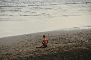 Man does a supine twist to stretch before surfing. 