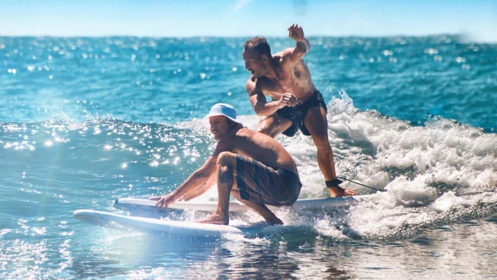 An image of two male surfers in the sea on surfboards working their upper body muscles